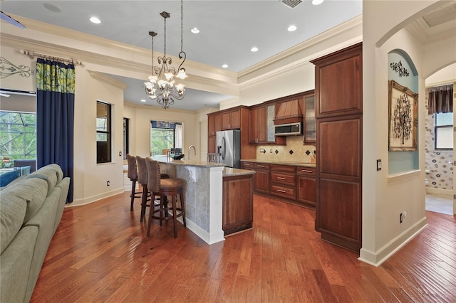 kitchen featuring decorative backsplash, a breakfast bar, a kitchen island with sink, stainless steel appliances, and a wealth of natural light