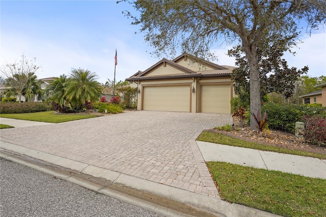 view of front facade with a garage, decorative driveway, a tile roof, and stucco siding