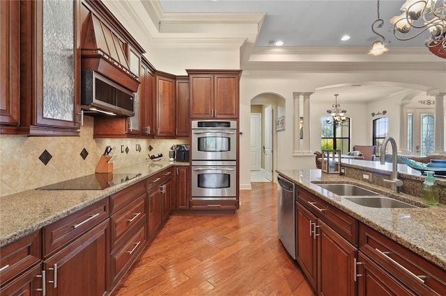 kitchen with arched walkways, appliances with stainless steel finishes, ornamental molding, a sink, and ornate columns