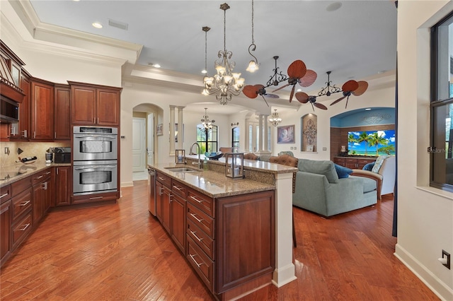 kitchen with arched walkways, backsplash, stainless steel double oven, a sink, and wood finished floors