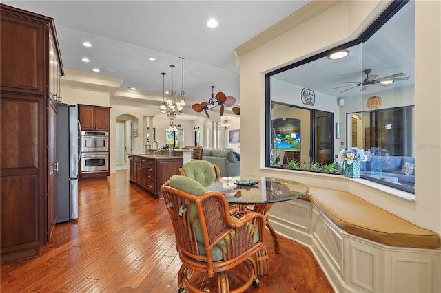 dining room with ceiling fan with notable chandelier, arched walkways, hardwood / wood-style floors, and recessed lighting