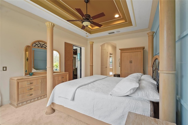 bedroom with arched walkways, light colored carpet, crown molding, a tray ceiling, and ornate columns