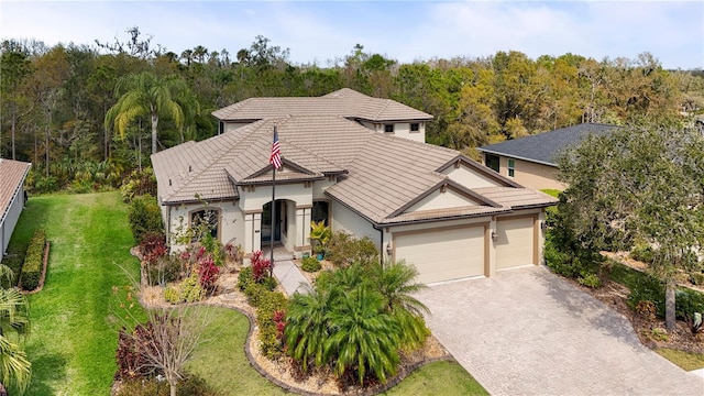 view of front of home with a tile roof, decorative driveway, stucco siding, a front lawn, and a wooded view