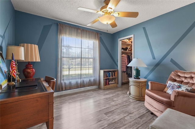 living area with ceiling fan, baseboards, a textured ceiling, and wood finished floors