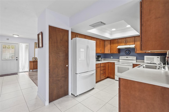 kitchen with white appliances, light tile patterned floors, a tray ceiling, light countertops, and under cabinet range hood