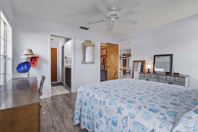 bedroom featuring visible vents, ensuite bath, wood finished floors, baseboards, and a spacious closet