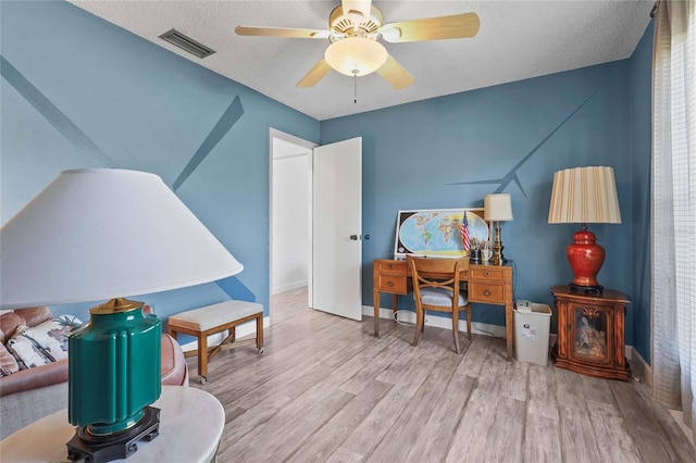 interior space featuring visible vents, a textured ceiling, wood finished floors, baseboards, and ceiling fan