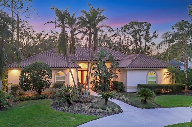 mediterranean / spanish-style home with a tiled roof, a front yard, and stucco siding