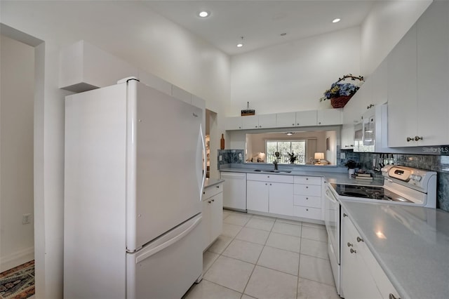 kitchen with white appliances, tasteful backsplash, light tile patterned floors, white cabinets, and a towering ceiling