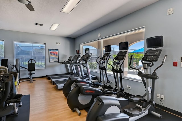 exercise room featuring light wood-type flooring, baseboards, visible vents, and a textured ceiling