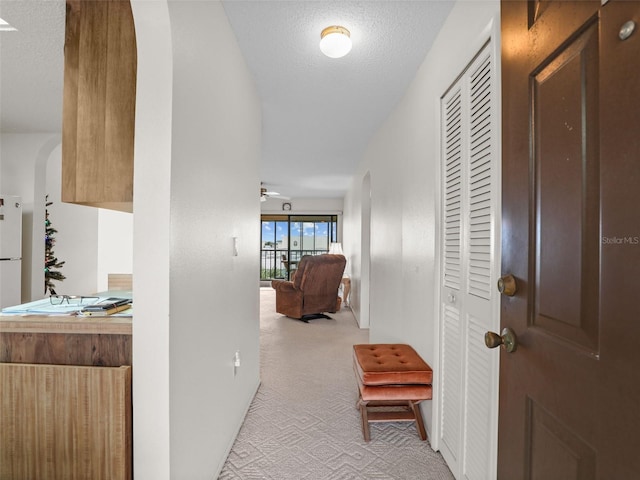 hall featuring arched walkways, light carpet, and a textured ceiling