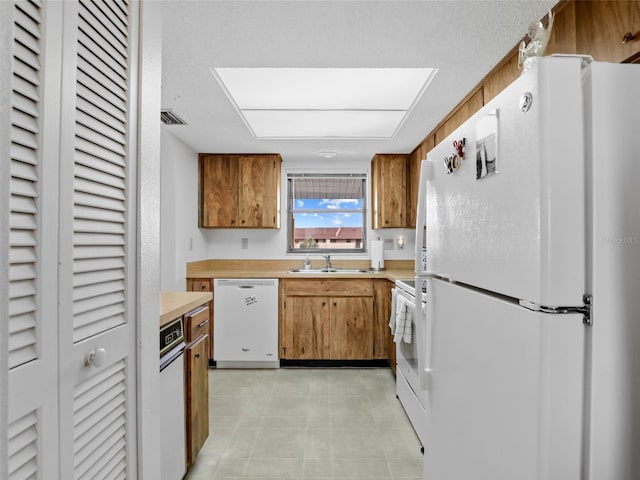 kitchen with white appliances, a sink, visible vents, light countertops, and brown cabinets