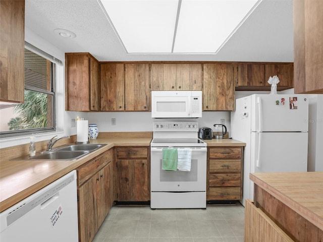 kitchen featuring light countertops, white appliances, a sink, and brown cabinets