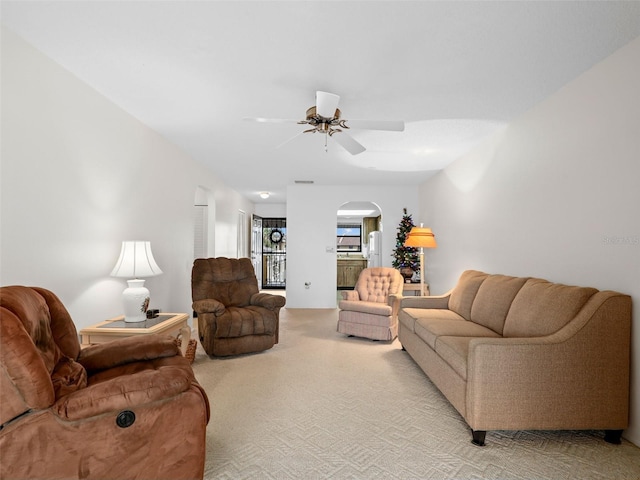 living area with light carpet, ceiling fan, and arched walkways