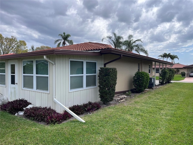 view of home's exterior featuring a yard, central AC unit, and a tiled roof