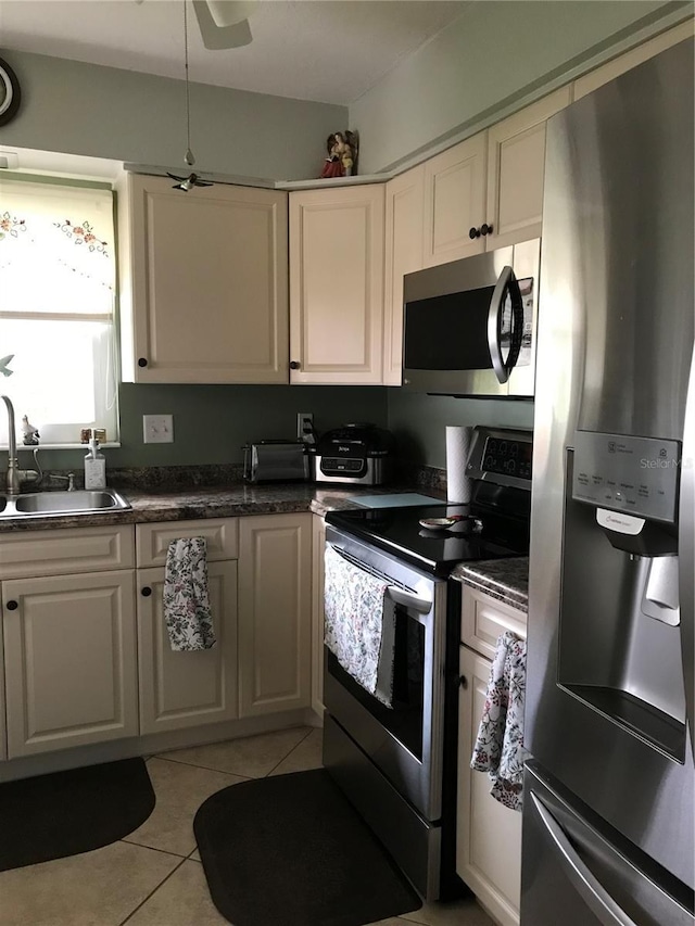 kitchen featuring light tile patterned floors, dark countertops, appliances with stainless steel finishes, white cabinets, and a sink