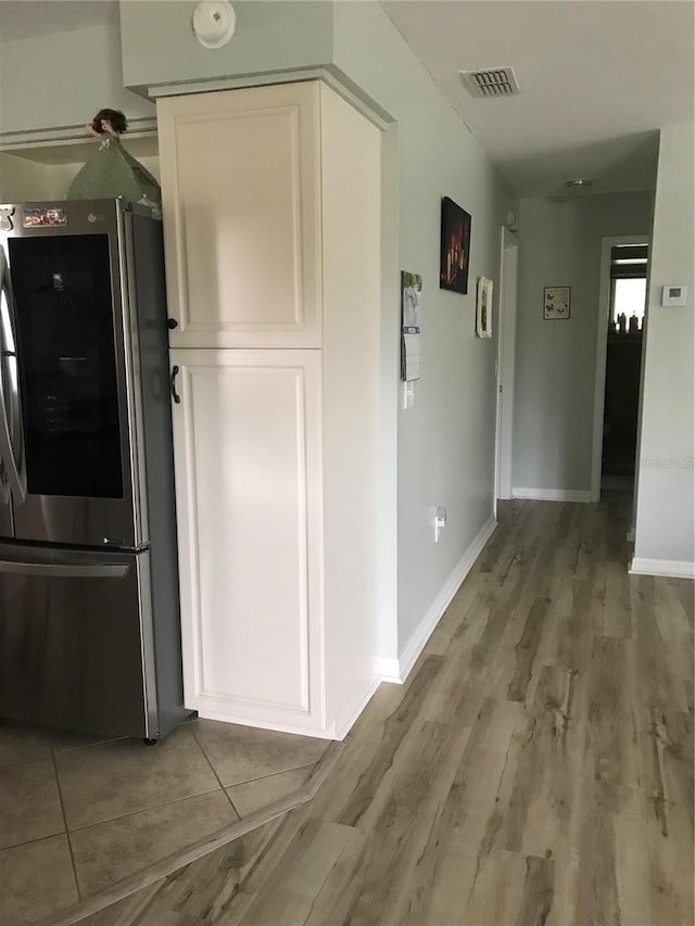 hallway with wood finished floors, visible vents, and baseboards