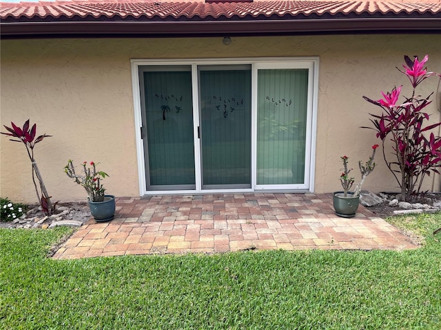 doorway to property featuring a tiled roof, a patio, a lawn, and stucco siding