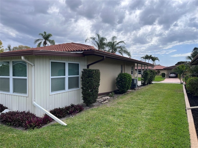 view of side of property featuring central AC, a lawn, and a tile roof