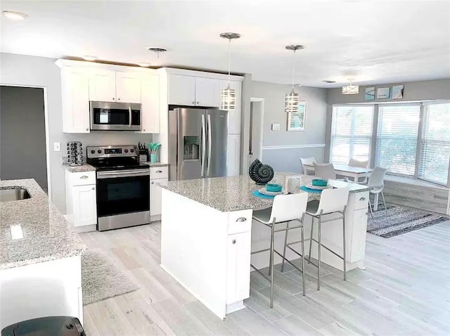 kitchen featuring light stone counters, pendant lighting, stainless steel appliances, white cabinets, and an island with sink