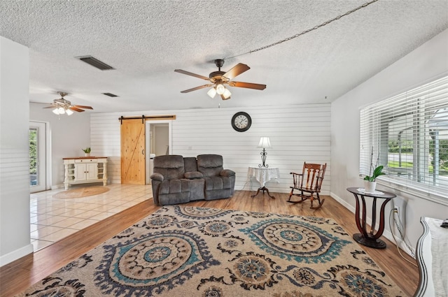 living room featuring visible vents, a barn door, a ceiling fan, a textured ceiling, and wood finished floors