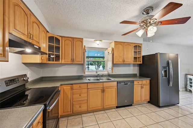 kitchen featuring a textured ceiling, under cabinet range hood, a sink, appliances with stainless steel finishes, and glass insert cabinets