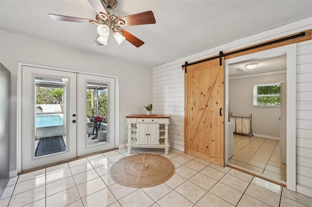 doorway with french doors, light tile patterned floors, a barn door, ceiling fan, and a textured ceiling