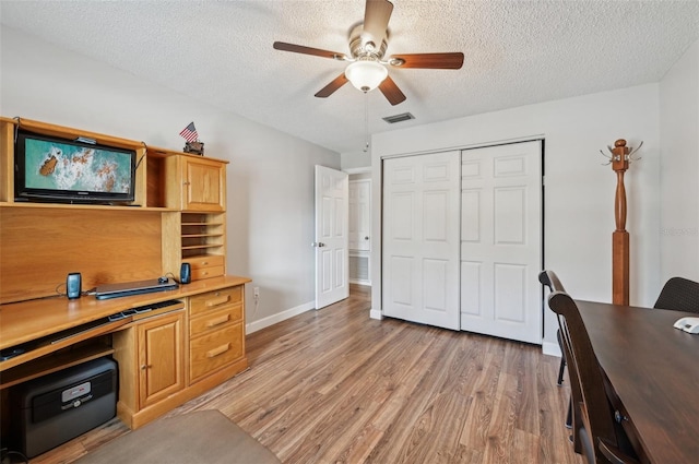 office area with a textured ceiling, a ceiling fan, baseboards, visible vents, and light wood-style floors