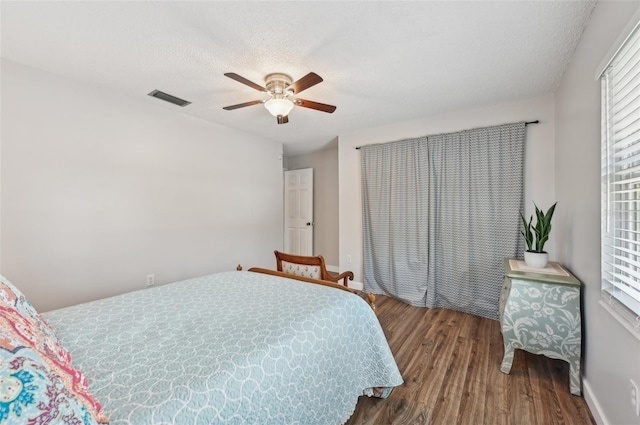 bedroom with a textured ceiling, ceiling fan, wood finished floors, and visible vents