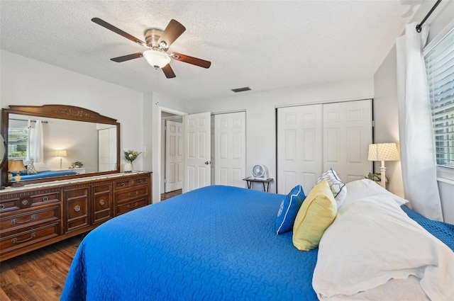 bedroom with visible vents, ceiling fan, dark wood-type flooring, a textured ceiling, and two closets