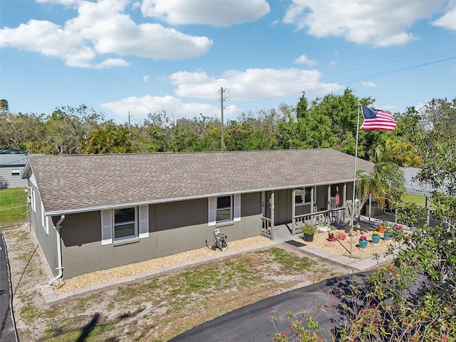 ranch-style home with a porch, roof with shingles, and stucco siding