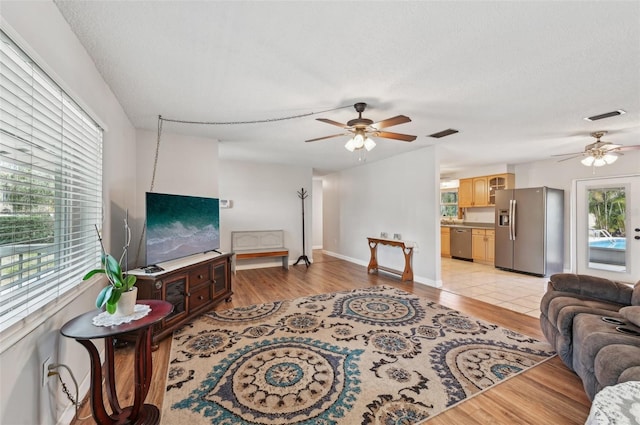 living room featuring light wood-style flooring, visible vents, and ceiling fan