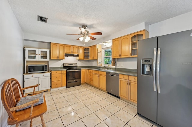 kitchen featuring stainless steel appliances, dark countertops, visible vents, a sink, and under cabinet range hood