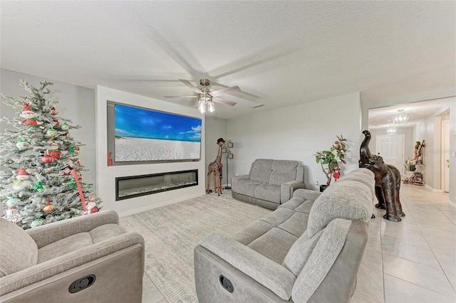 living area with a textured ceiling, ceiling fan, light tile patterned floors, and a glass covered fireplace