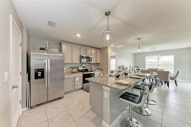 kitchen with pendant lighting, appliances with stainless steel finishes, an island with sink, and gray cabinetry