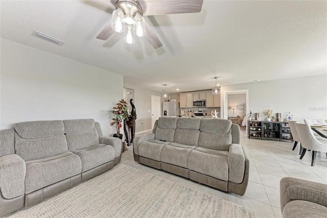 living area featuring a textured ceiling, light tile patterned flooring, visible vents, and a ceiling fan