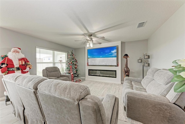 living room with ceiling fan, a textured ceiling, visible vents, baseboards, and a glass covered fireplace