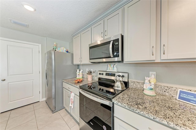 kitchen with light tile patterned floors, visible vents, light stone countertops, stainless steel appliances, and a textured ceiling