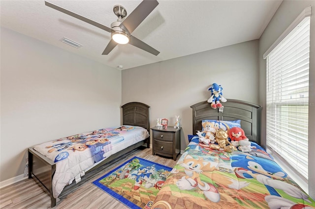 bedroom featuring ceiling fan, wood finished floors, visible vents, and baseboards