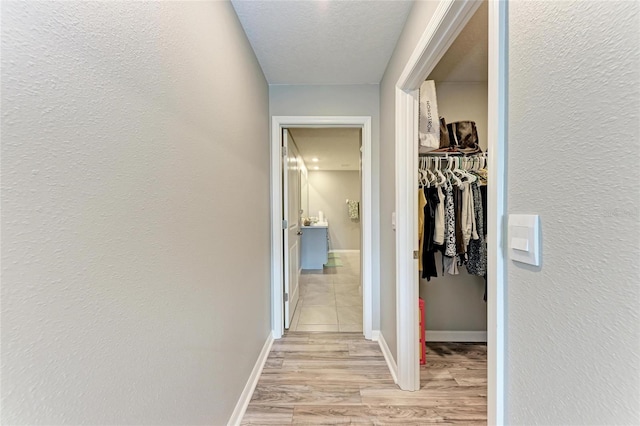 corridor with baseboards, a textured wall, a textured ceiling, and light wood finished floors