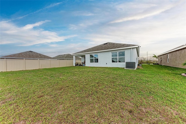 rear view of house with stucco siding, fence, central AC, and a yard