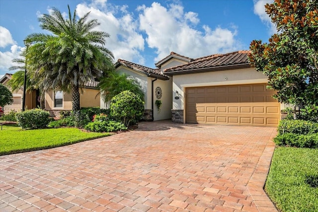 mediterranean / spanish-style home with stone siding, a tiled roof, an attached garage, decorative driveway, and stucco siding