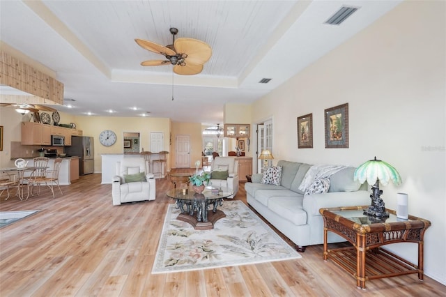 living area with light wood finished floors, visible vents, a raised ceiling, and a ceiling fan