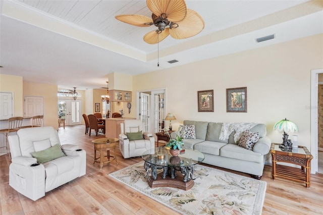 living area featuring light wood finished floors, visible vents, a tray ceiling, and ceiling fan with notable chandelier