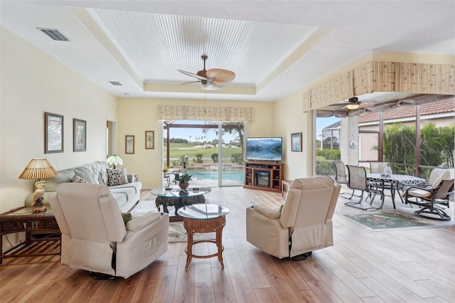 living room with a tray ceiling, visible vents, ceiling fan, and wood finished floors