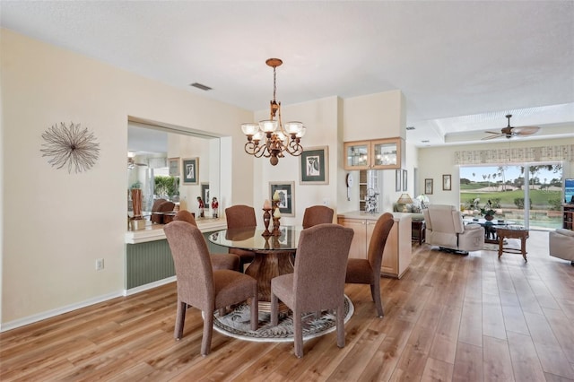 dining room featuring baseboards, visible vents, a tray ceiling, light wood-type flooring, and ceiling fan with notable chandelier