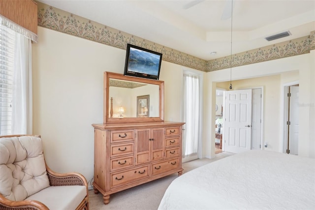 bedroom with a tray ceiling, multiple windows, visible vents, and light colored carpet