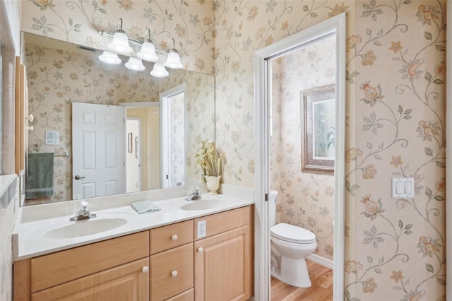 full bathroom featuring wood finished floors, a sink, toilet, and wallpapered walls