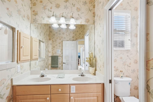 full bathroom with toilet, wallpapered walls, double vanity, and a sink