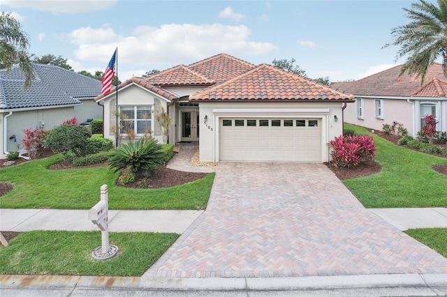 mediterranean / spanish house featuring a tile roof, an attached garage, decorative driveway, a front lawn, and stucco siding